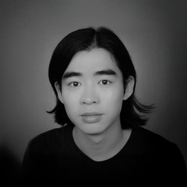 黒い服を着た黒髪の人物のバストアップのモノクロ写真