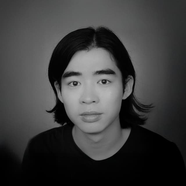 黒い服を着た黒髪の人物のバストアップのモノクロ写真